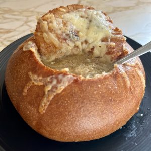 a bread bowl with the top cut out filled with soup and a spoon in it