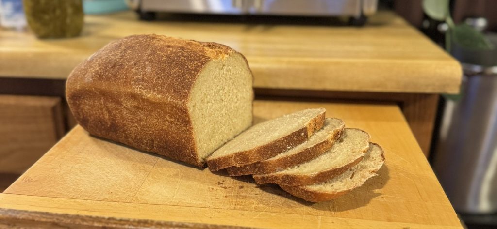 A halfway sliced loaf of bread sitting atop a cutting board