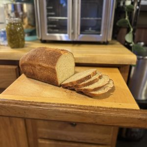 A halfway sliced loaf of bread sitting atop a cutting board with a countertop oven in the background.
