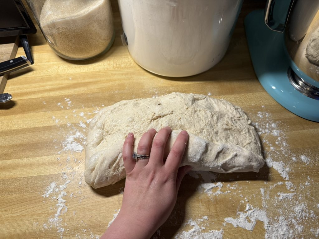 a hand with a ring halfway through rolling up the dough along the long side.